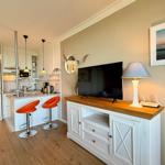 Living area with TV stand, lamp, and kitchen area with orange bar stools.