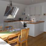Küche mit Essbereich, Holztisch, Stühle, Dunstabzugshaube und Fenster