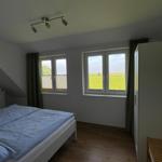Schlafzimmer mit Doppelbett, Holzboden und Fenster zur grünen Landschaft.