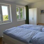 Schlafzimmer mit Doppelbett, zwei Fenstern und weißem Schrank.