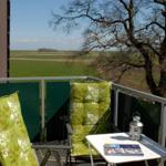 Balkon mit zwei grünen Stühlen und Tisch. Blick auf Feld und Baum.