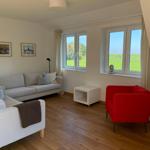 Wohnzimmer mit Sofa, rotem Sessel und Blick auf grünes Feld.