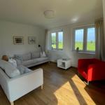 Wohnzimmer mit Sofa, rotem Sessel und Blick auf grünes Feld.