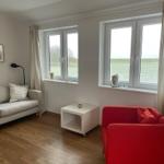 Wohnzimmer mit Sofa, rotem Sessel und Blick auf Felder