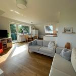 Wohn- und Essbereich mit Sofa, TV und Terrasse. Holzboden und Fenster.