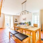 Esszimmer mit Holztisch, Stühlen und Treppenhaus. Terrassentür und Wohnbereich sichtbar.