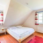 Schlafzimmer mit Doppelbett, zwei Fenstern und Holzboden.