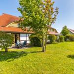 Haus mit Terrasse, Garten und Bäumen unter blauem Himmel.