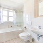 Badezimmer mit Badewanne, Dusche, Waschbecken und Toilette. Fenster mit Vorhängen.