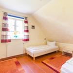 Zimmer mit zwei Betten, Fenster mit Vorhängen und Heizkörper an der Wand.