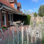 Terrasse mit Tisch, Stühlen und Markisen. Holzzaun und Sandstrand im Hintergrund.