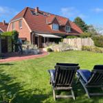 Haus mit Garten, zwei Liegestühle und Terrasse unter Sonnenschutz.