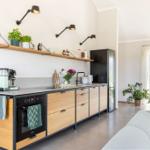 Moderne Küche mit Holzschränken, Kühlschrank und Arbeitsfläche. Wohnbereich mit Sofa und Pflanzen.