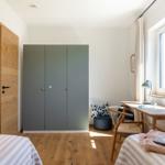 Schlafzimmer mit Doppelbett, Kleiderschrank und Schreibtisch am Fenster.