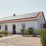 Moderne Villa mit Solaranlage, Terrasse und gepflastertem Hof. Grünflächen und Hecken umgeben das Haus.