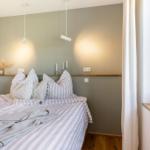 Schlafzimmer mit Bett, Fenster und moderner Beleuchtung.