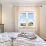 Schlafzimmer mit Bett, Fenster und Kleiderschrank. Draußen ist ein Feld mit blauem Himmel.