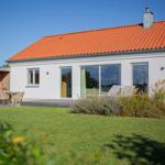 Wohnhaus mit Terrasse, Garten und Holzsauna. Große Fenster und roter Dachziegel.