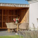 Holzterrasse mit Tisch, Stühlen und Blumenarrangement vor einem Gartenhaus.