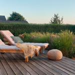 Terrasse mit zwei Liegestühlen, Decke und Kissen. Hintergrund: grüner Heckenzaun und Blumenbeete.