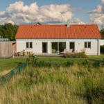 Moderne Villa mit rotem Dach, Terrasse und Garten. Holzhaus nebenan.