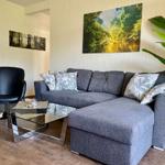 Ein Wohnzimmer mit grauem Sofa, Glas-Tisch und Wandbildern.