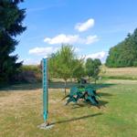 Green garden with table, chairs, and umbrella. Background: meadow and trees.
