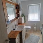 Bathroom with sink, toilet, and shower. Wooden countertop and window with curtains.