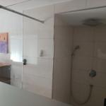 Shower with handheld showerhead and glass enclosure, next to kitchenette with wooden countertop.