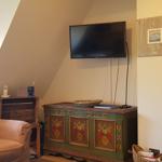 Wohnzimmer mit Sessel, Fernseher und dekorativem Schrank.