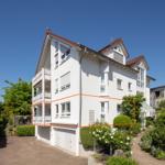 Weiße Maisonette-Wohnung mit Balkon und Gartenbereich. Modernes Design mit rotem Dachziegel.