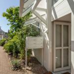 Eingangsbereich mit Glastür, Briefkasten und gepflasterter Weg durch grünen Garten.