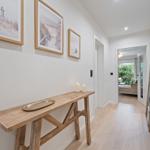 Hallenbereich mit Holztisch, Kerzen und Bildern an der Wand. Durchgang zu Wohnbereich mit Gartenansicht.