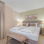 Schlafzimmer mit Doppelbett, zwei Nachttischen und Fenster mit Vorhang.