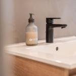 Waschbecken mit schwarzer Wasserhahn und Seifenspender auf Holzunterschrank