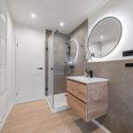 Badezimmer mit Dusche, Waschbecken und runden Spiegel.
