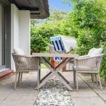 Terrasse mit Tisch und Stühlen, Strandkorb und grüner Umgebung.