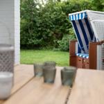 Terrasse mit Holztisch, Strandkorb und Garten.