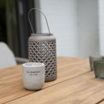 Holztisch mit Kerze, Laterne und Gläsern im Außenbereich.