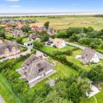 Dorf mit strohgedeckten Häusern und grünen Wiesen bis zum Strand.