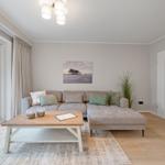 Wohnzimmer mit Sofa, Couchtisch und großem Fenster. Wandbild und Pflanze sichtbar.
