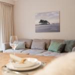 Wohnzimmer mit Sofa, Tisch und Wandbild. Fenster mit Vorhängen.