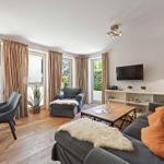 Living and dining area with sofa, coffee table, and TV. Wooden floor and large windows.