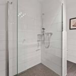 Shower with glass enclosure, white tiles, and handheld shower. Two pictures hang on the wall.