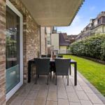 Terrace with table and chairs beside a glass front and green lawn.