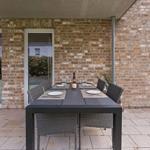 Terrace with set dining table and wine bottle against brick wall.