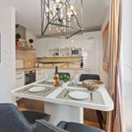 Dining area with table, chairs, and view into the kitchen. Ceiling light and window with curtains.