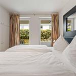 Bedroom with double bed, white linens, and view of balcony with greenery.