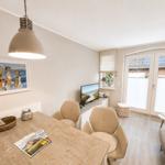 Essbereich mit Holztisch, Stühlen und Fernseher. Fenster mit Jalousien und Wandbild.