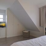 Schlafzimmer mit Dachschräge, Bett, Schrank, TV und Fenster mit Vorhängen.